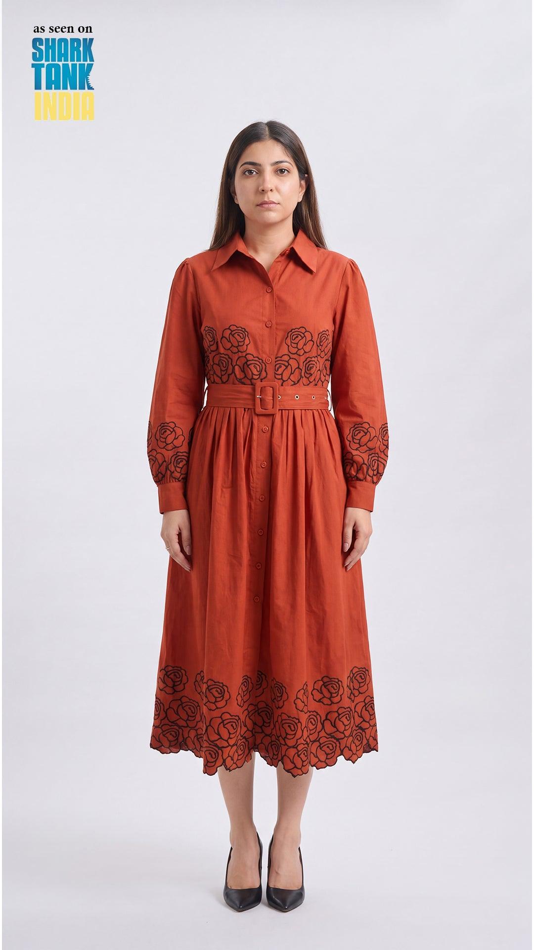Woman wearing a rust-colored dress with floral embroidery on a white background