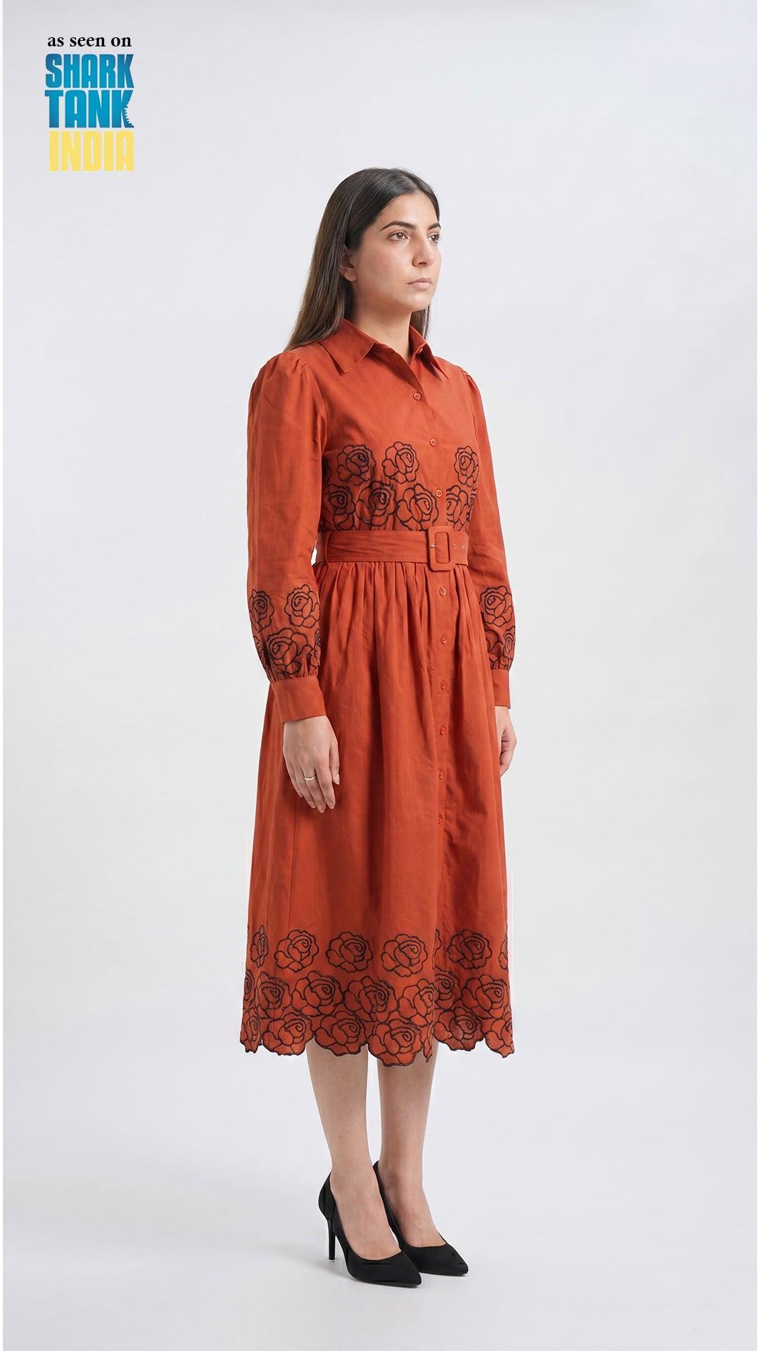 Woman wearing a rust-colored dress with floral embroidery on a white background