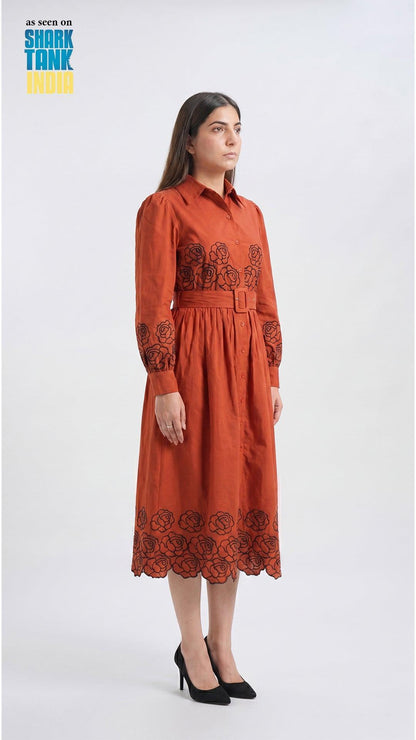 Woman wearing a rust-colored dress with floral embroidery on a white background