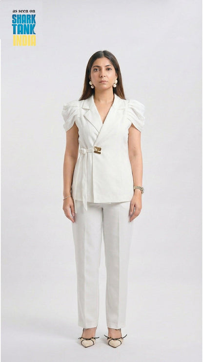 Woman wearing a white outfit with a blazer and pants on a plain background