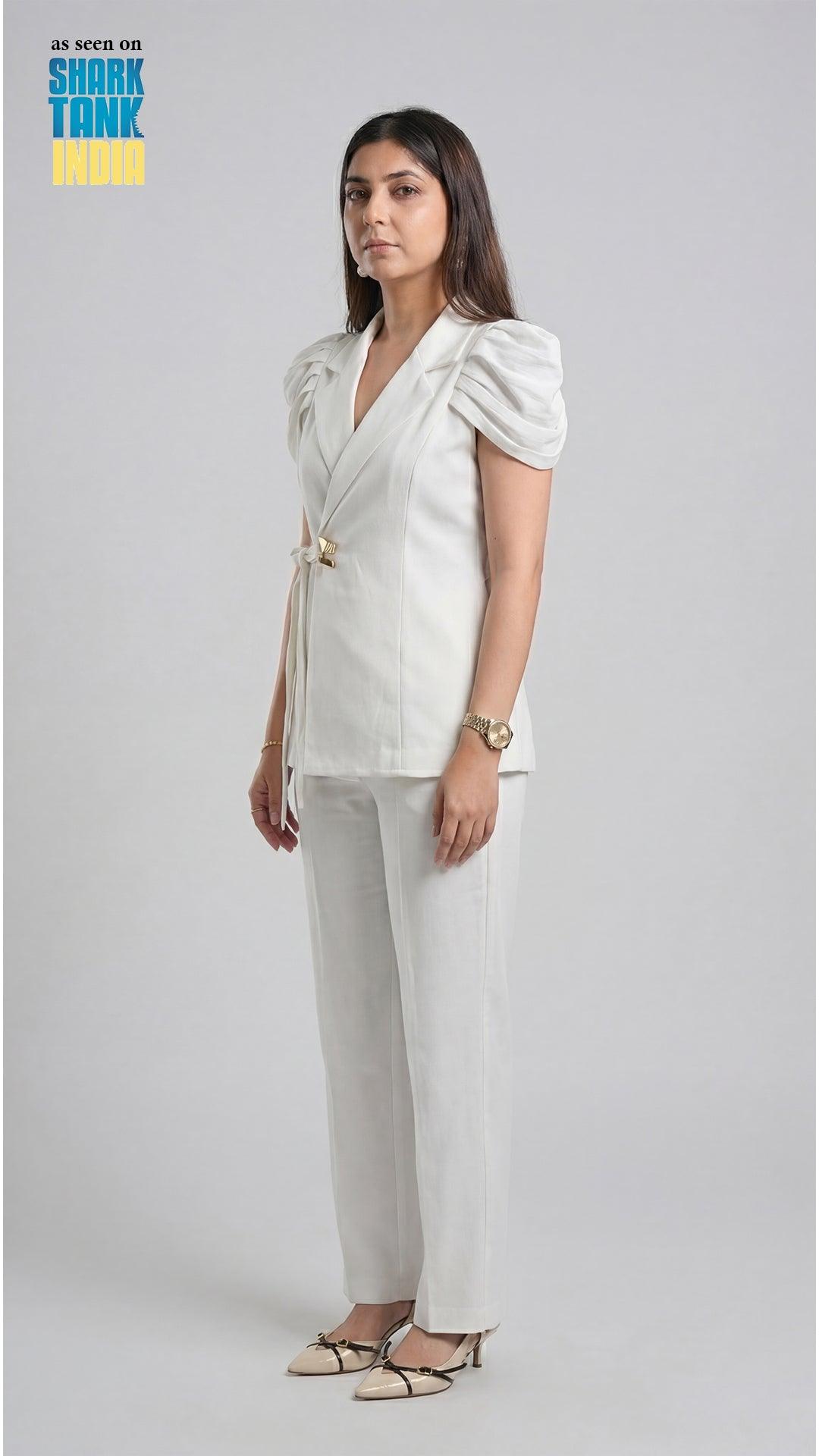 Woman wearing a white outfit with a blazer and pants on a plain background