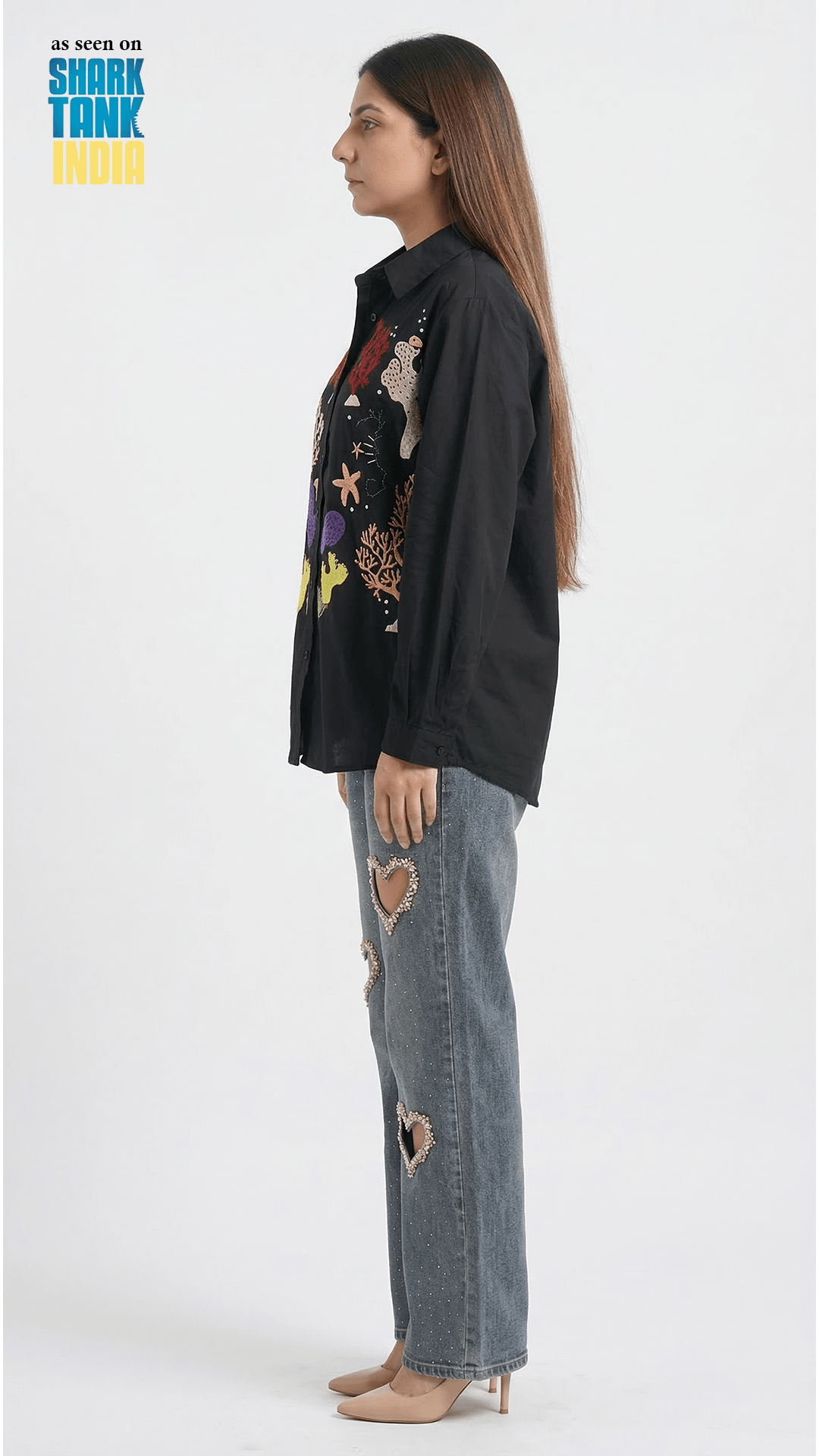 Woman wearing a black shirt with colorful floral embroidery and ripped jeans on a white background