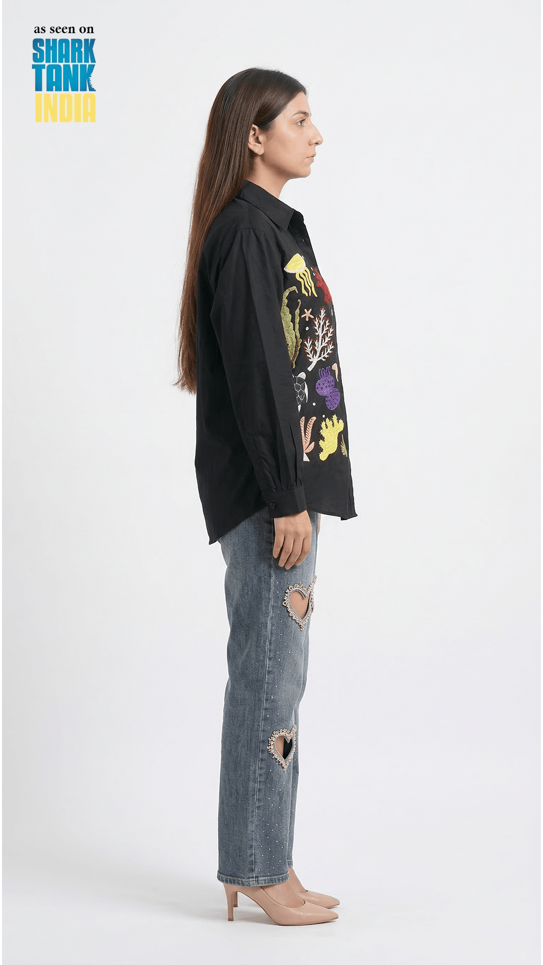 Person wearing a black shirt with colorful graphics and ripped jeans on a white background