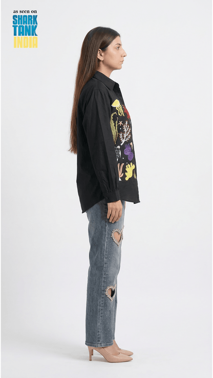 Person wearing a black shirt with colorful graphics and ripped jeans on a white background