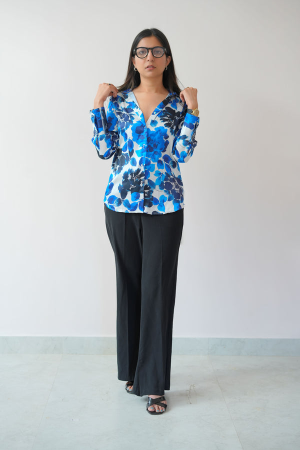 A woman modeling a satin shirt with a blue floral print, standing against a plain background.