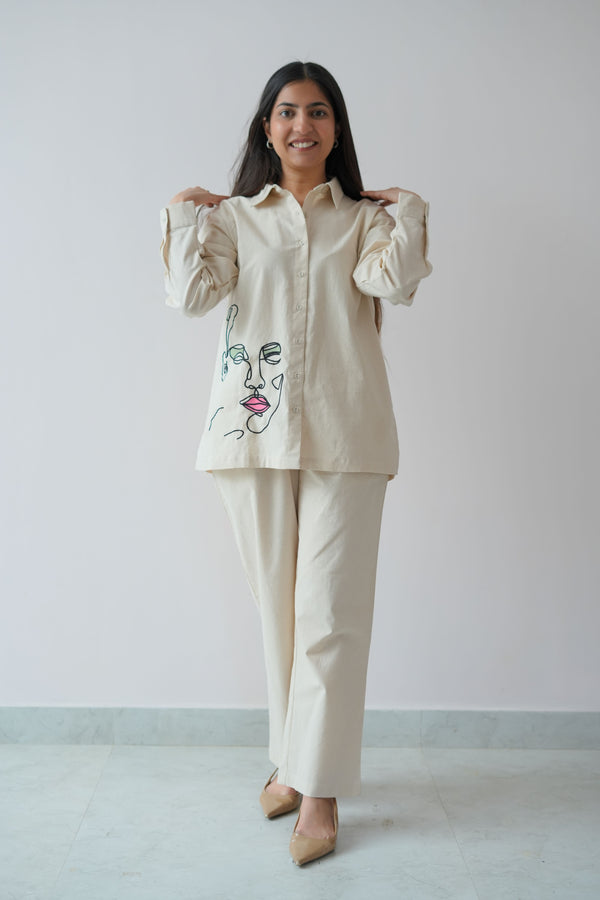 A woman wearing a beige co-ord set with a Mona Lisa thread embroidery on the shirt, standing against a plain background.
