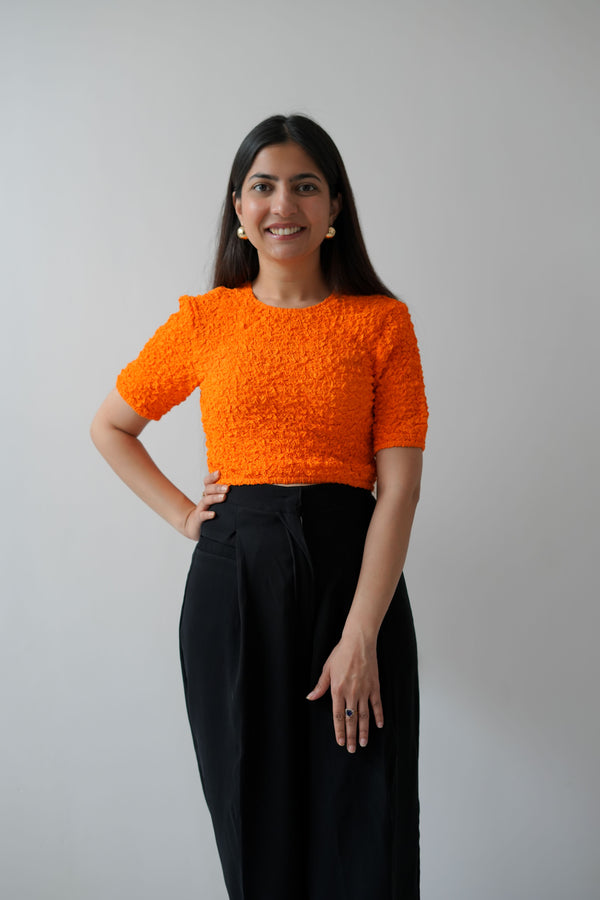 A person wearing a solid orange short-sleeved top with a round neckline and a smock pattern.