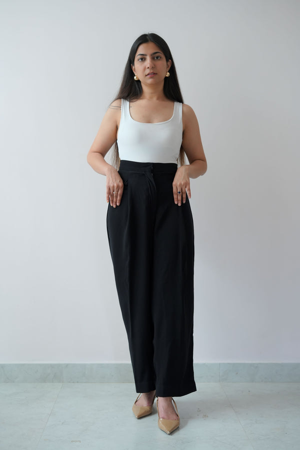 A person standing in a room wearing a white tank top and black pants, with no visible brand markings.