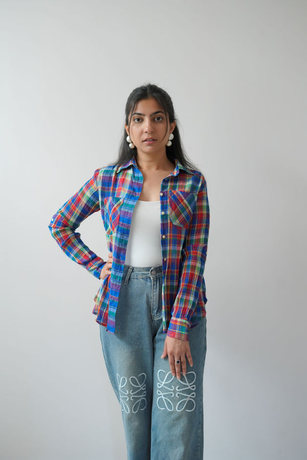 A person wearing a plaid shirt with red, blue, and white colors, and blue jeans with white floral patterns on the knees.