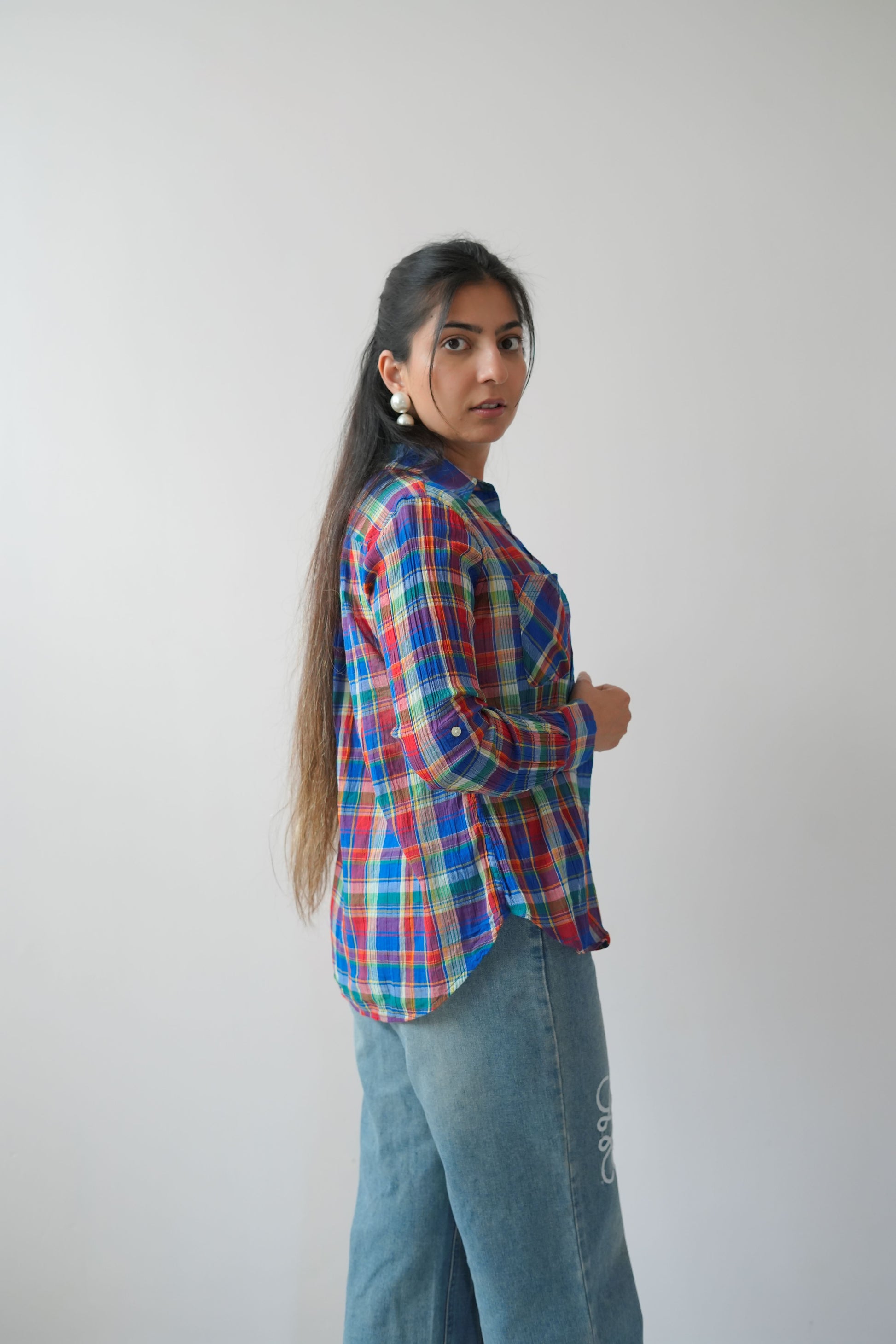 A person wearing a plaid shirt with red, blue, and white colors, and blue jeans with white floral patterns on the knees.