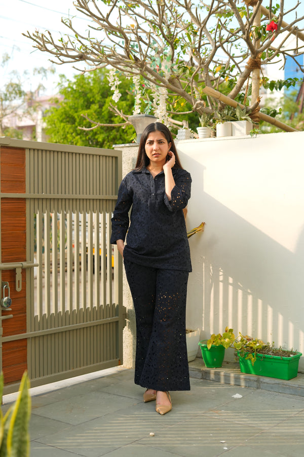 A woman wearing a white long-sleeve top with a classic collar and cutwork detailing, paired with matching white straight-leg pants.