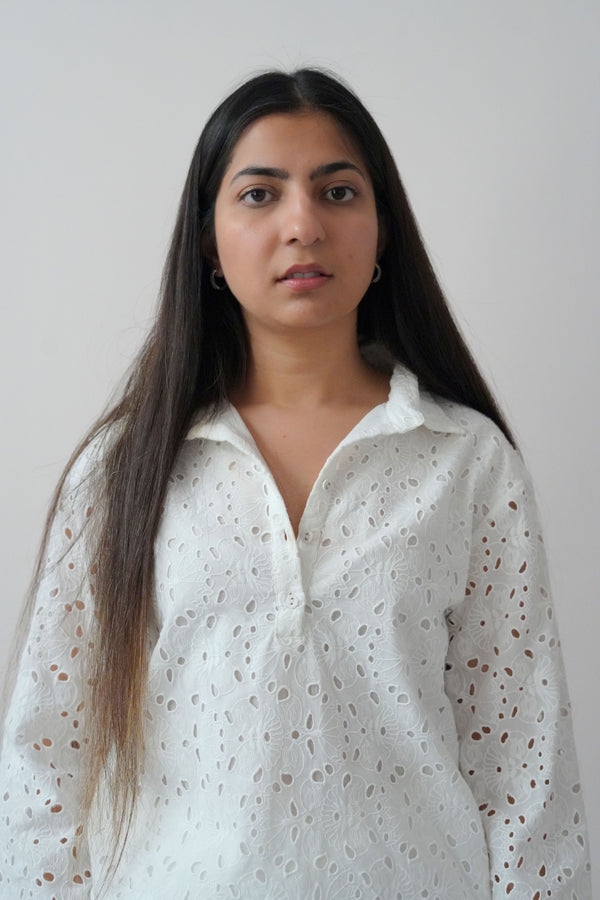 A woman wearing a white long-sleeve top with a classic collar and cutwork detailing, paired with matching white straight-leg pants.