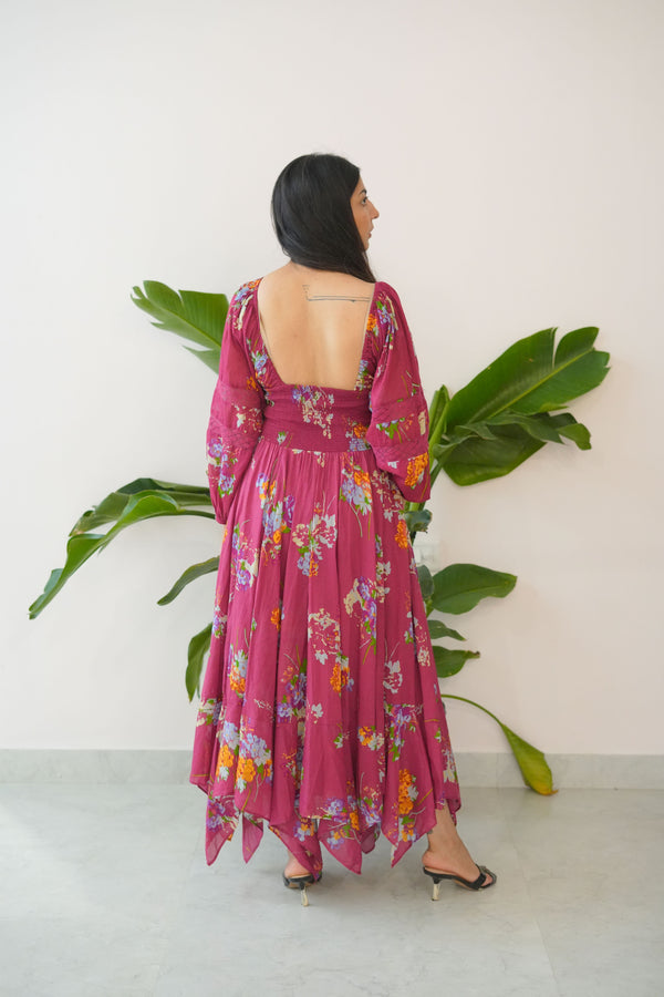 Person wearing a pink floral dress standing among green plants indoors.