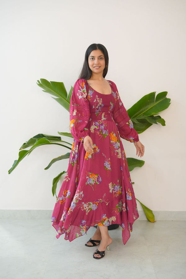 Woman in a pink floral dress standing next to a large green plant against a white wall.