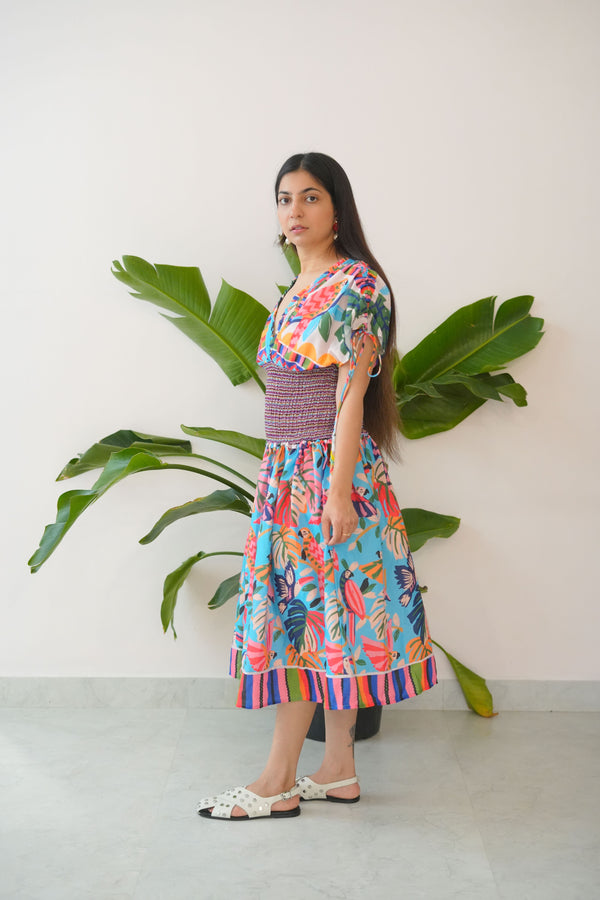 Woman wearing a colorful dress with a patterned skirt standing against a white wall.