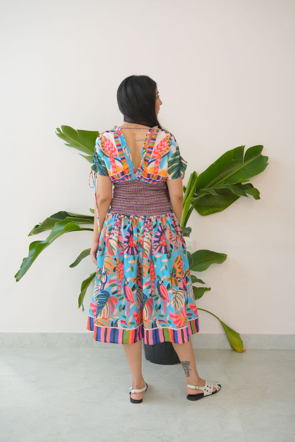 Person wearing a colorful dress standing in front of a plant against a white wall