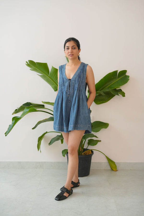 Woman in a blue dress standing next to a large green plant indoors.