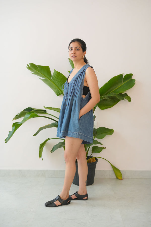 Woman in a blue dress standing next to a large green plant indoors.