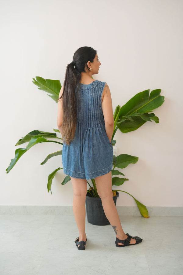 Woman in a denim dress standing next to a potted plant indoors.