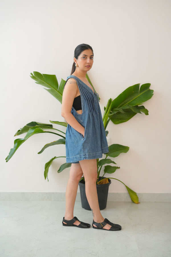 Woman in a denim dress standing next to a large green plant indoors.