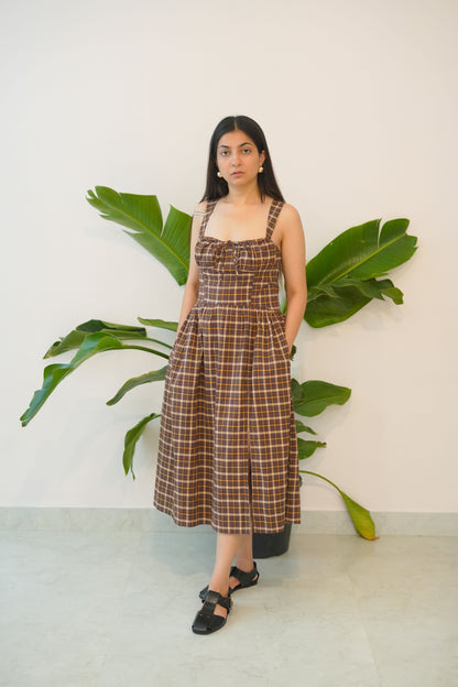 Woman in a plaid dress standing next to a large plant against a white wall.