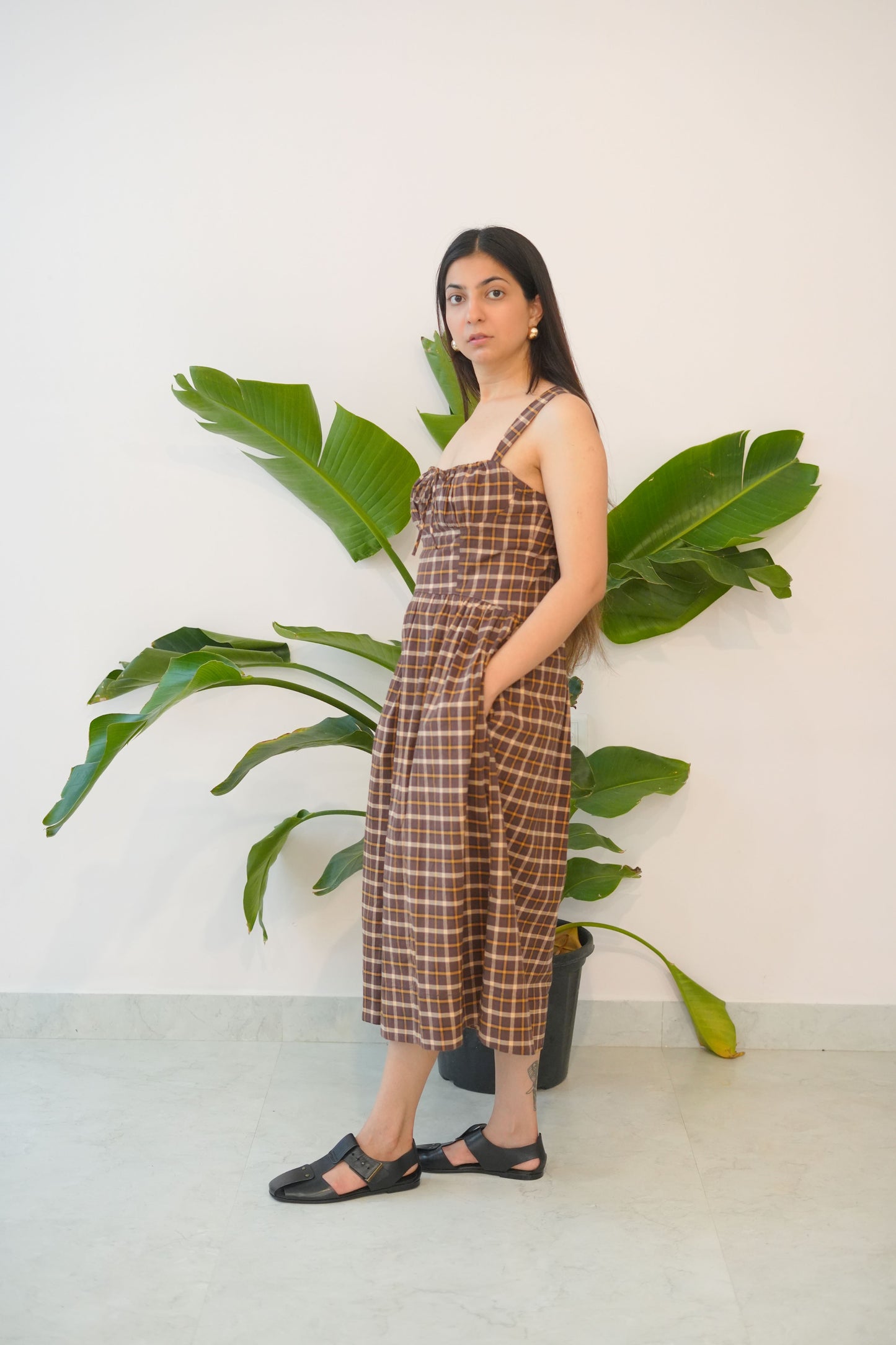 Woman in a plaid dress standing next to a large green plant indoors.