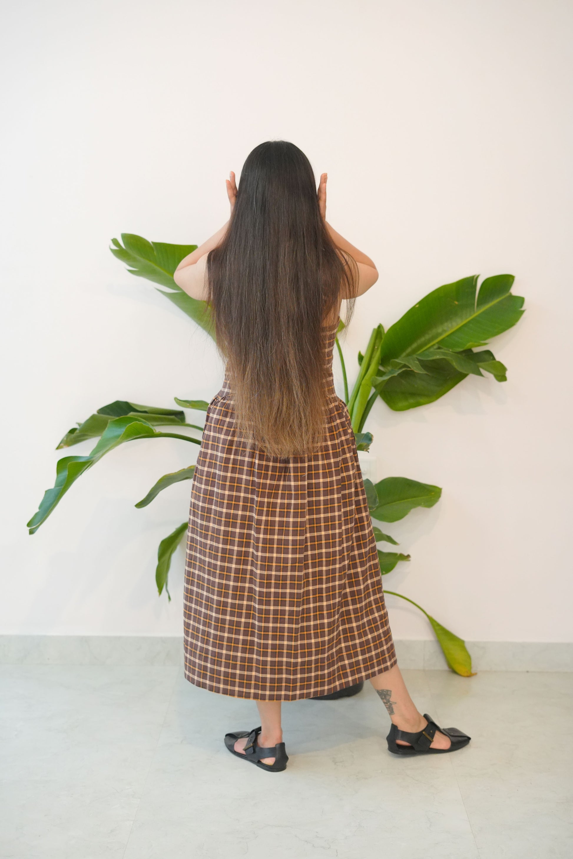 Person wearing a plaid skirt standing next to a potted plant on a white floor.