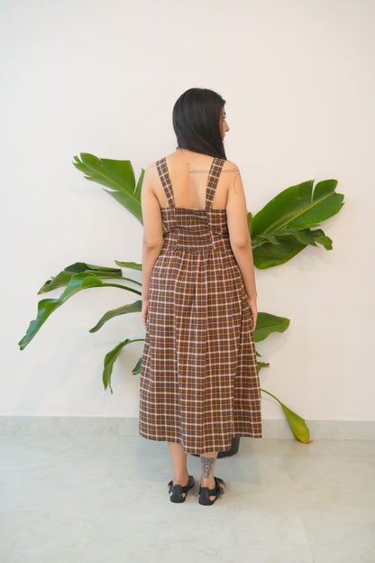 Person wearing a plaid dress standing next to a large green leafy plant indoors.
