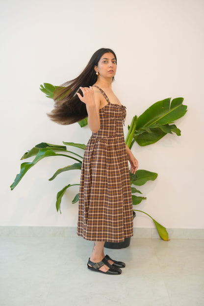 Woman in a plaid dress standing next to a plant against a white wall