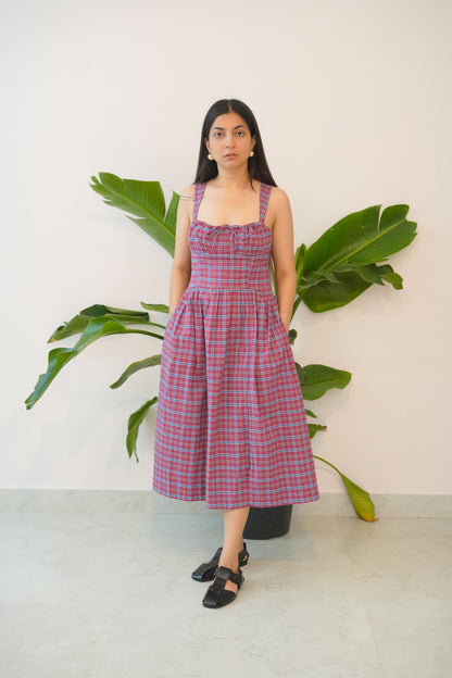 Woman wearing a red and white checkered dress standing in front of green plants.