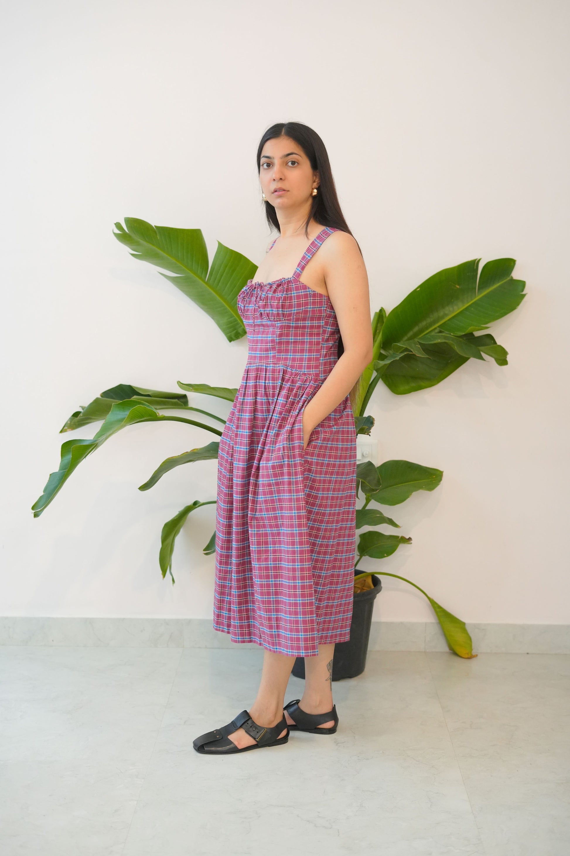 Woman in a red checkered dress standing among large green leaves on a white background