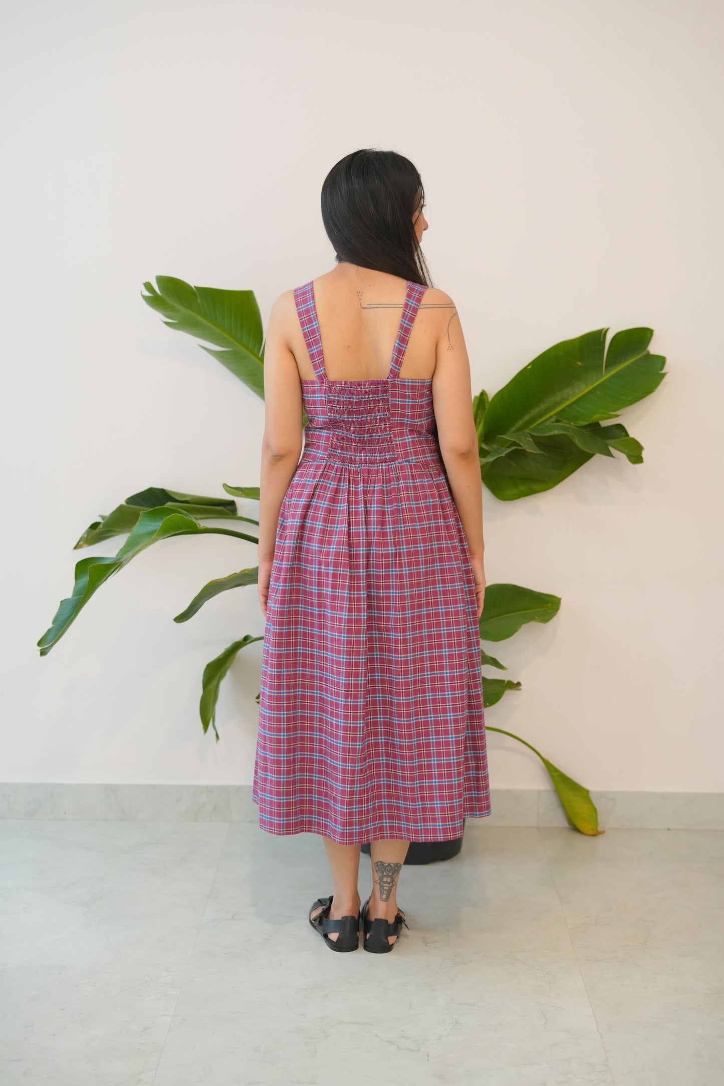 Person wearing a red and white checkered dress standing next to a plant against a light background