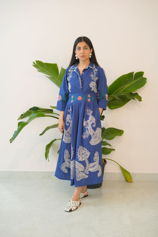 Person wearing a blue traditional outfit with white patterns, standing against a light background.