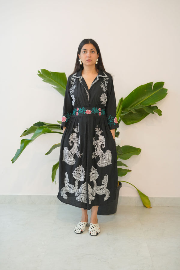 Black embroidered dress worn by a person with a plant in the background