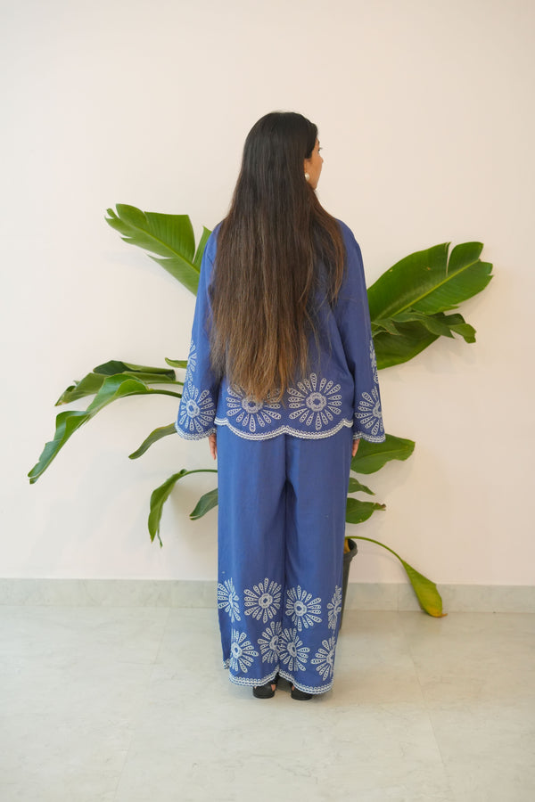 Person wearing a blue outfit with white floral patterns standing next to a plant.