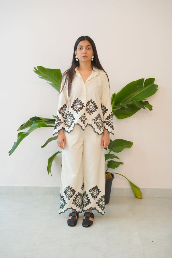 Person wearing a white dress with black floral patterns standing between two large green leaves.