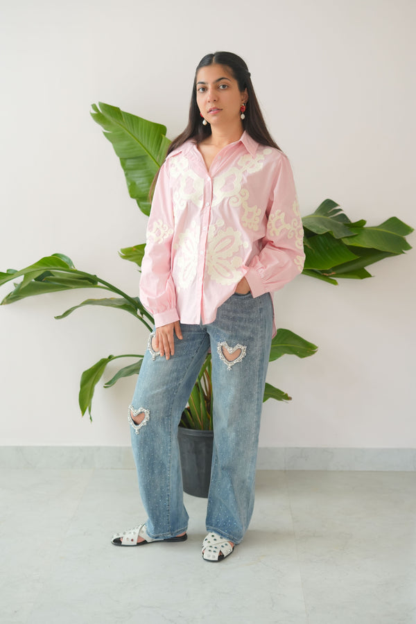 Person wearing a pink blouse and blue jeans standing among green plants indoors.