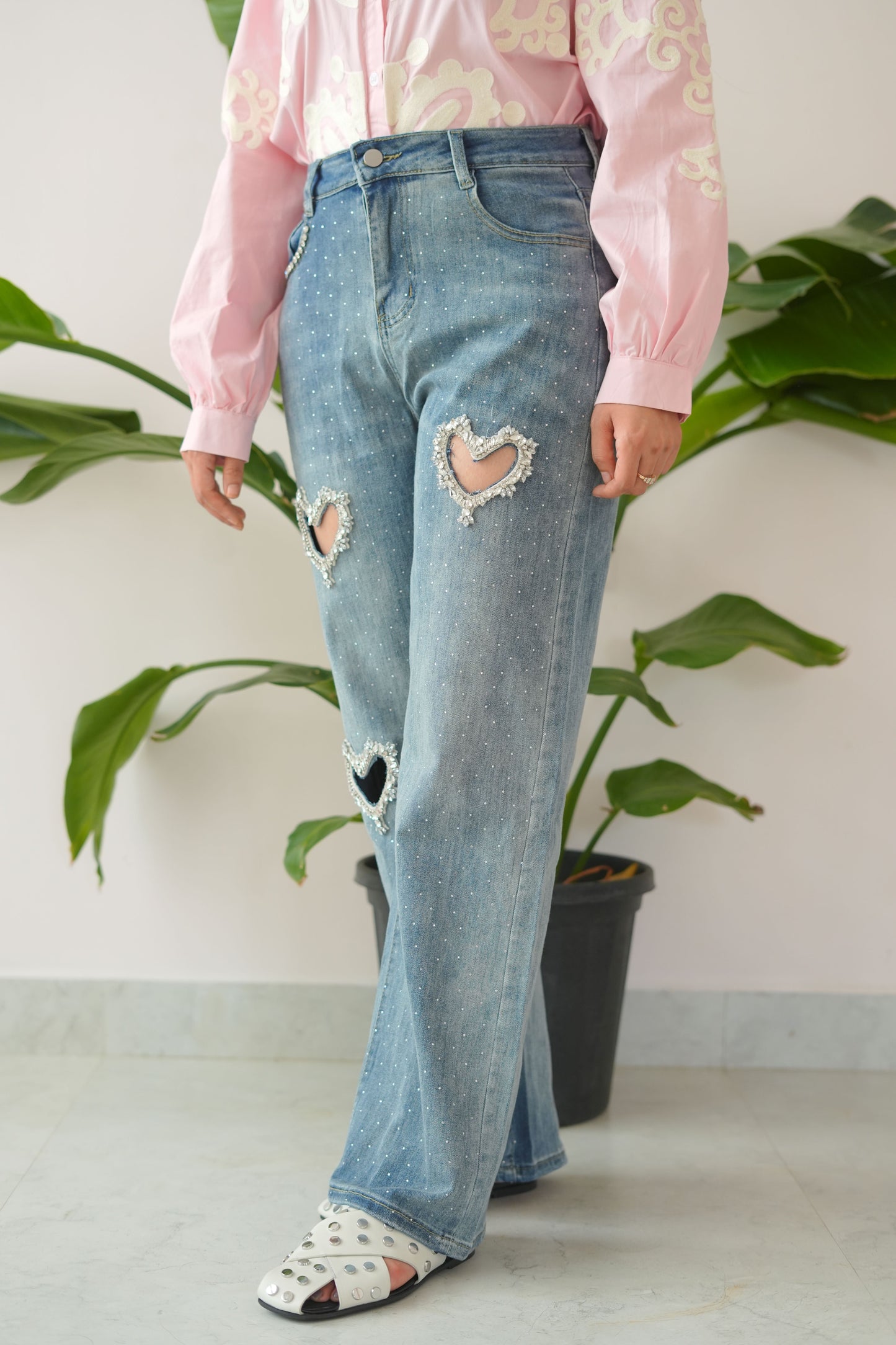 Person wearing ripped blue jeans and white sneakers standing on a plant
