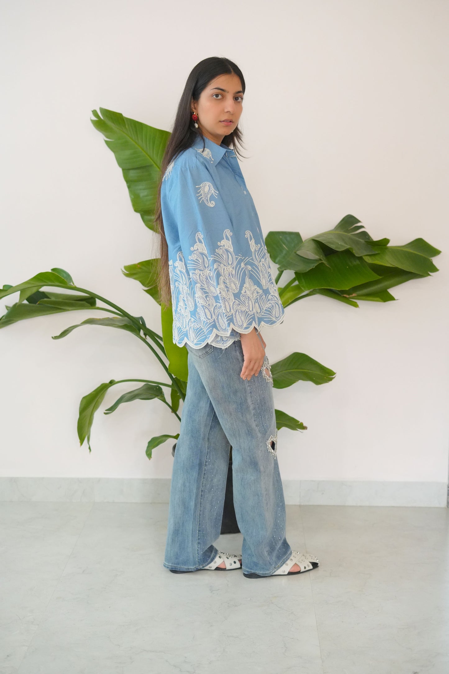Person wearing a blue denim outfit with white lace top, standing next to a large green plant indoors.