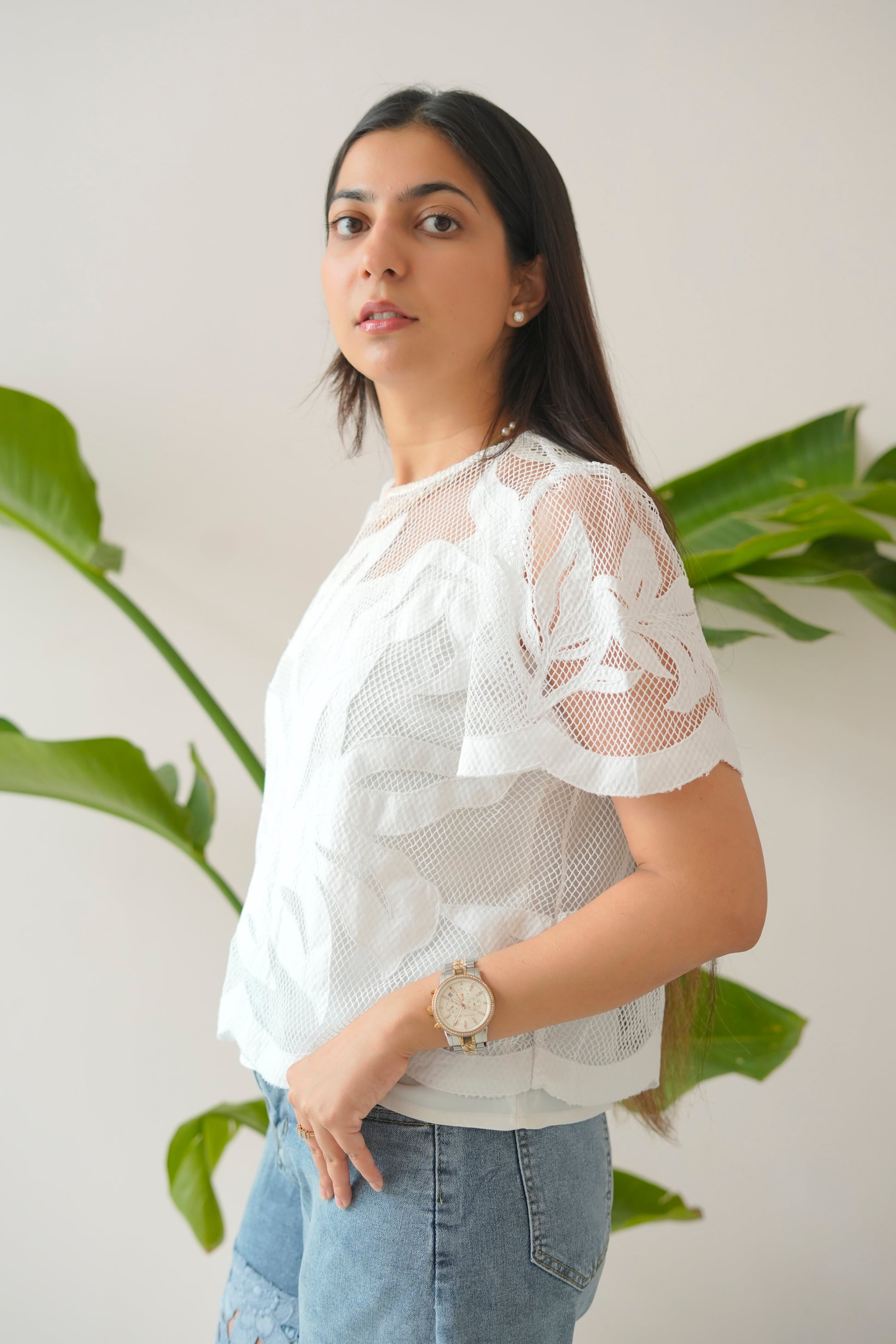 Woman wearing a white lace top and blue jeans with plants in the background