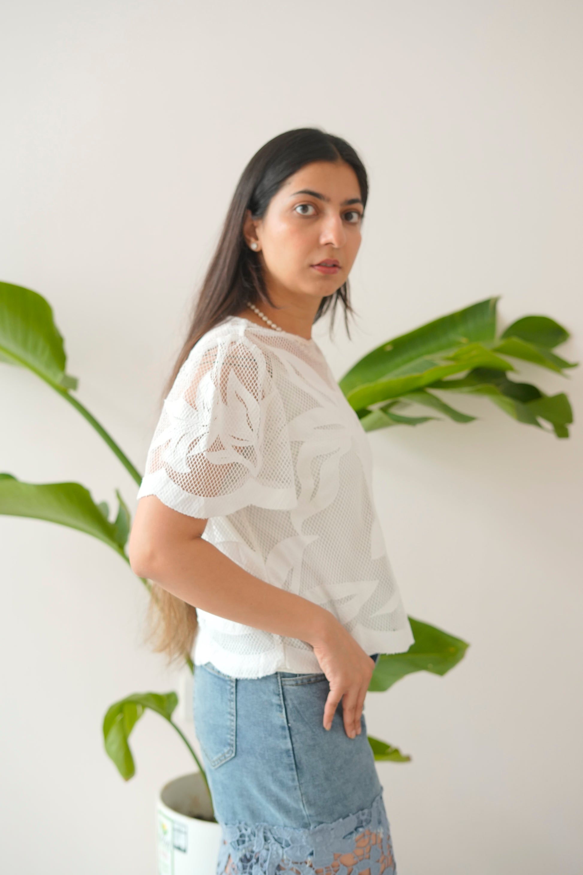 Woman wearing a white blouse and blue jeans standing in front of green plants.