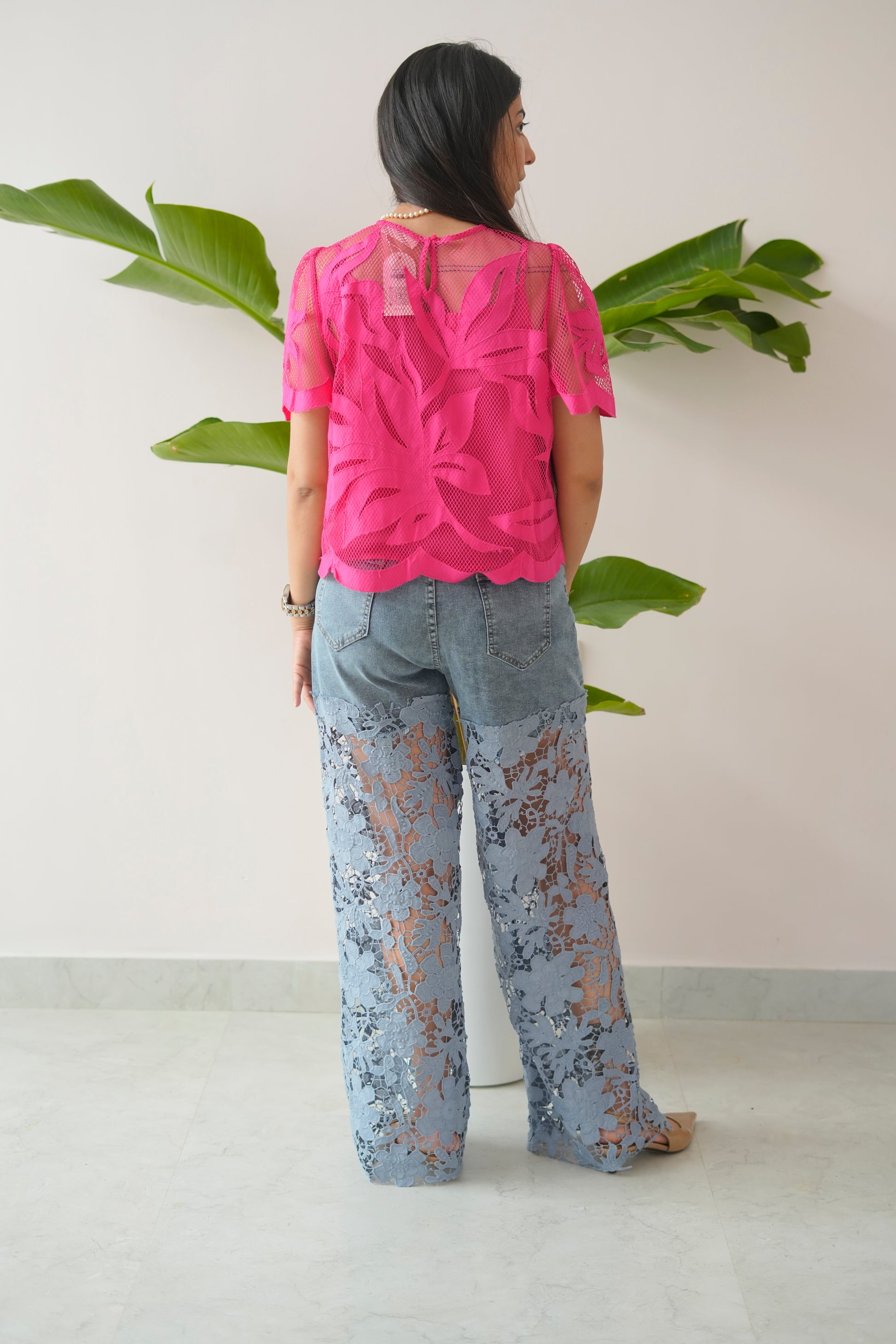 Person wearing a pink top and floral pants standing in front of a plant.