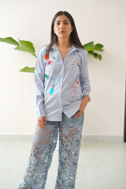 Woman wearing a light gray outfit with colorful patterns, standing indoors.