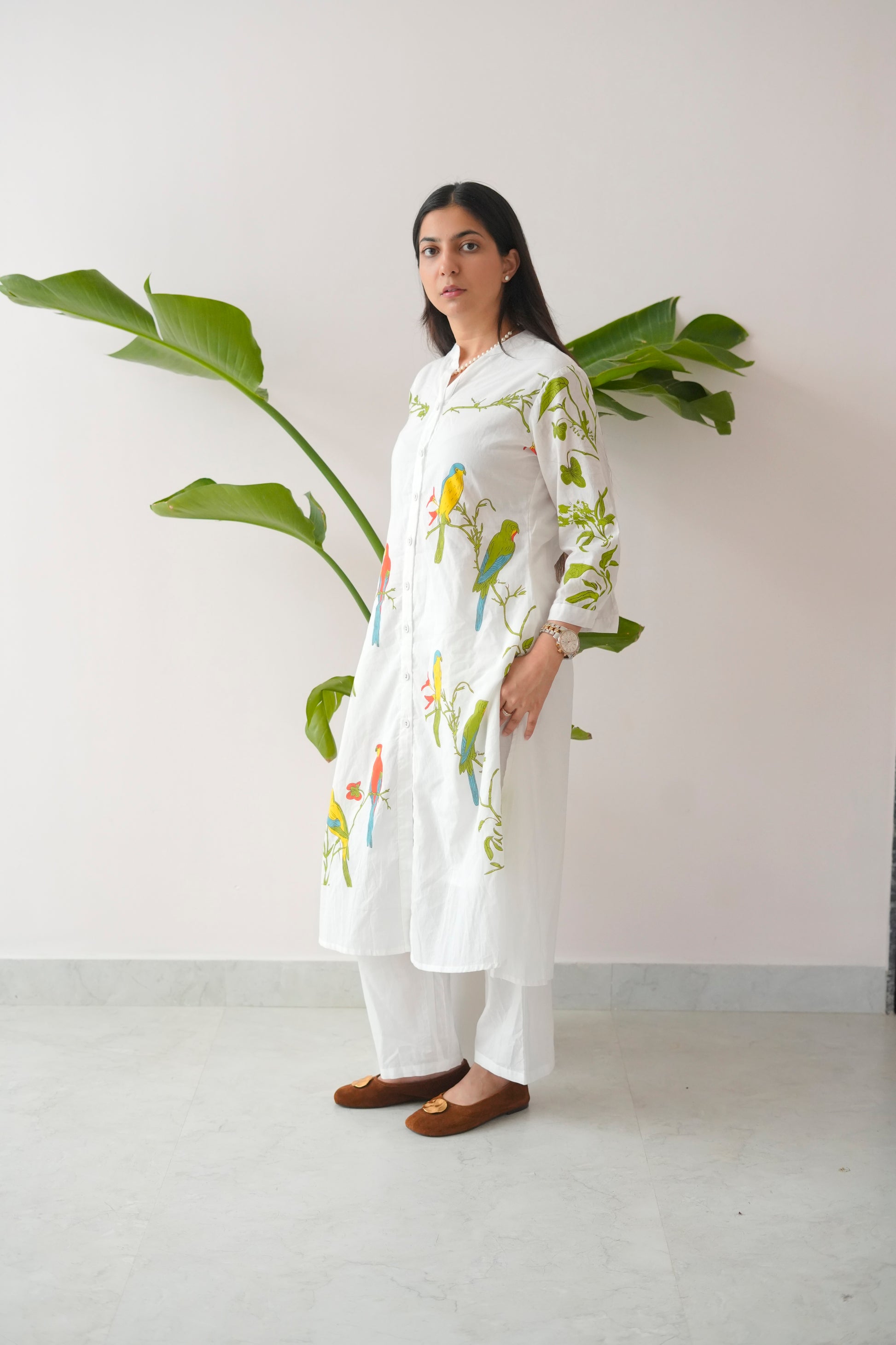 Woman wearing a white floral kurta with white pants standing against a light background