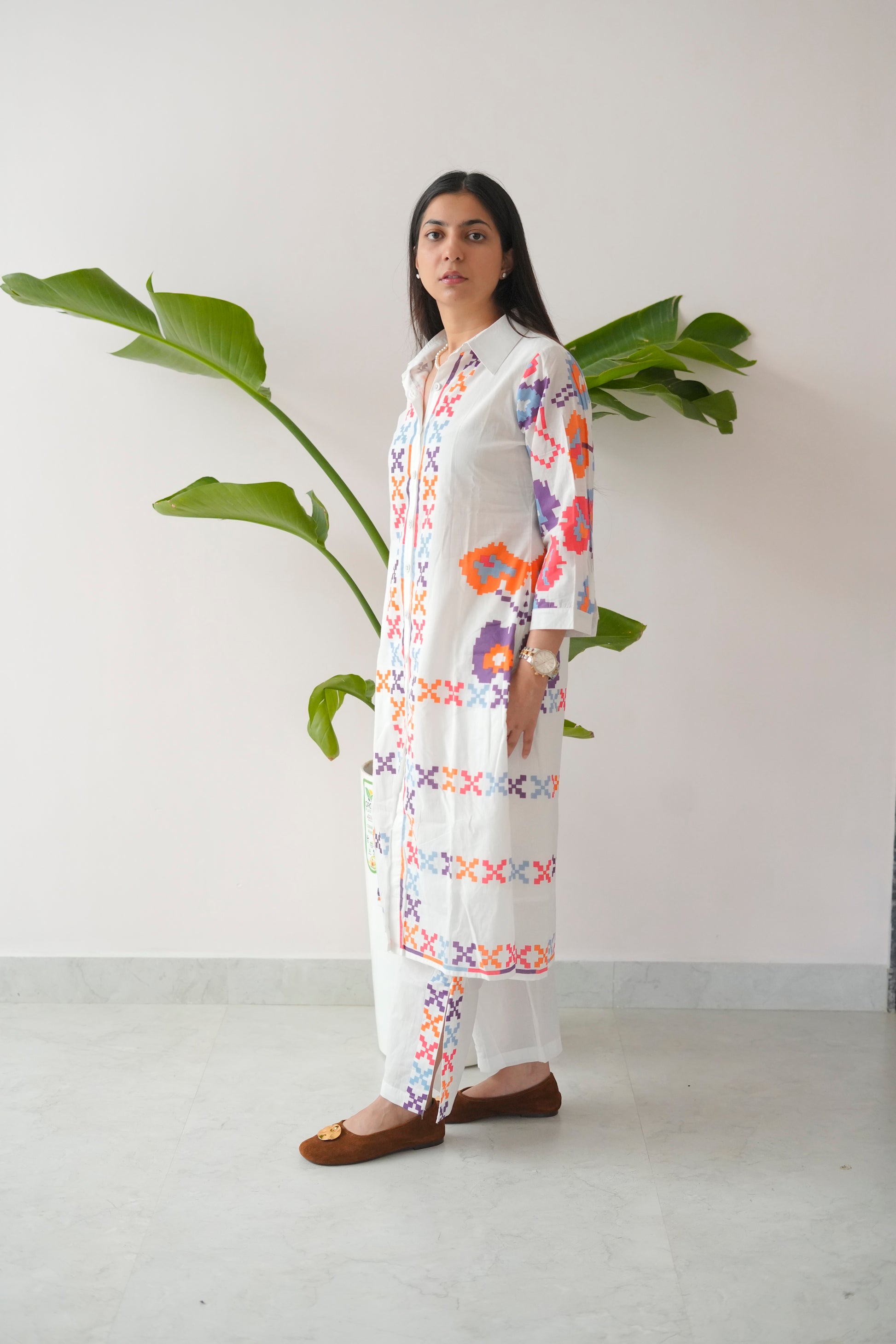 Woman wearing a long, white embroidered dress with colorful patterns against a plain background.