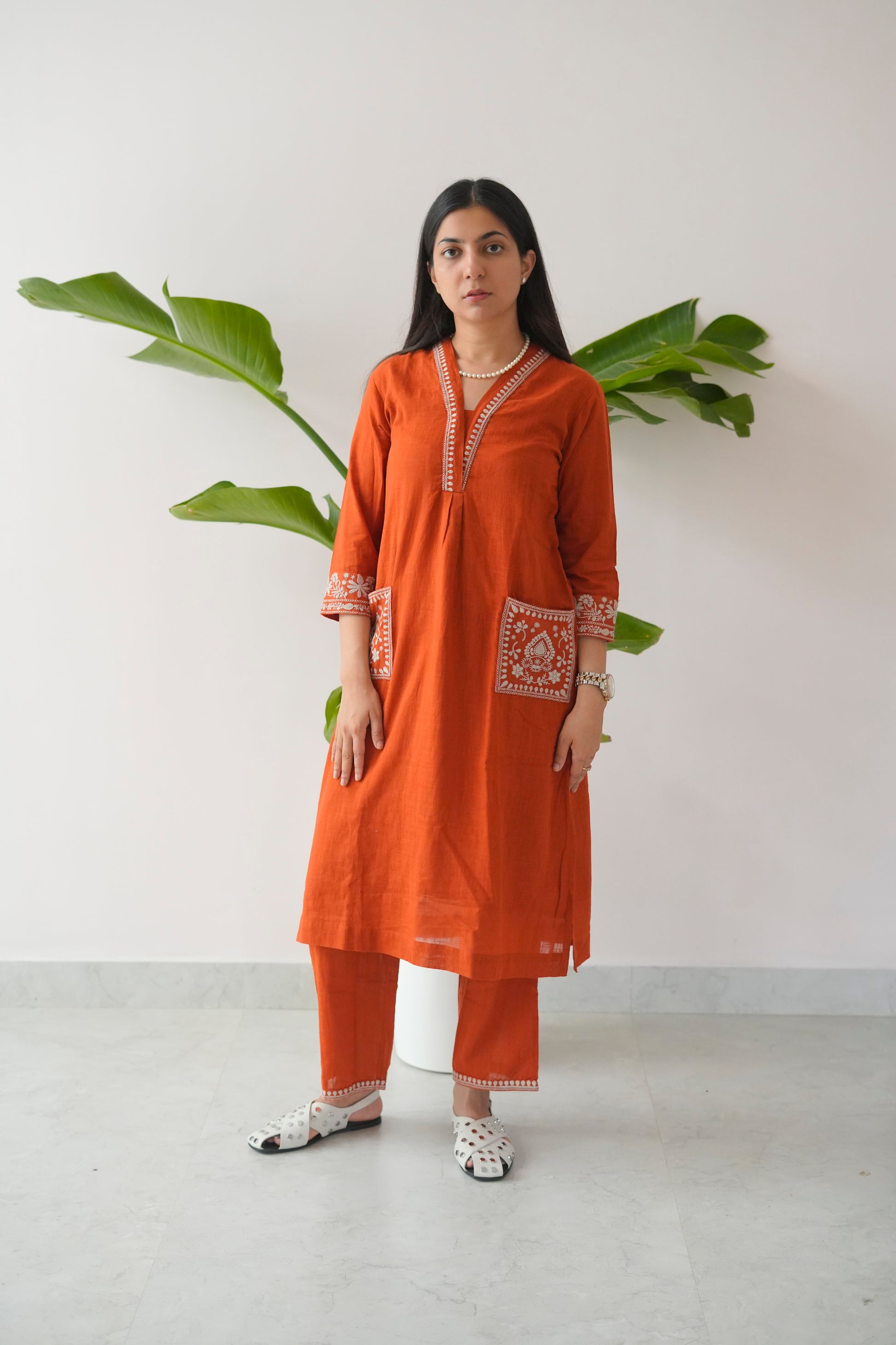 Woman wearing an orange traditional outfit with a white background and plant