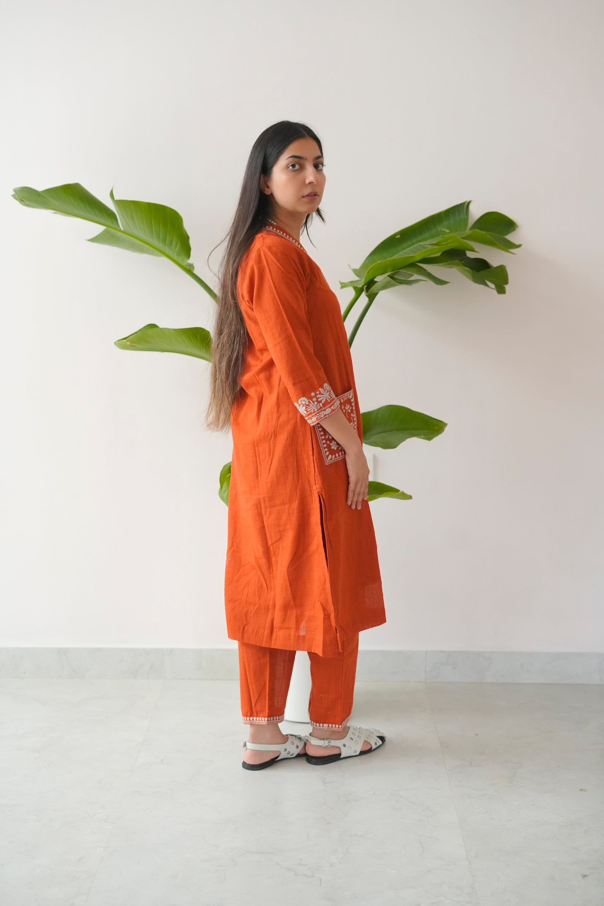 Woman wearing an orange outfit with a plant in the background