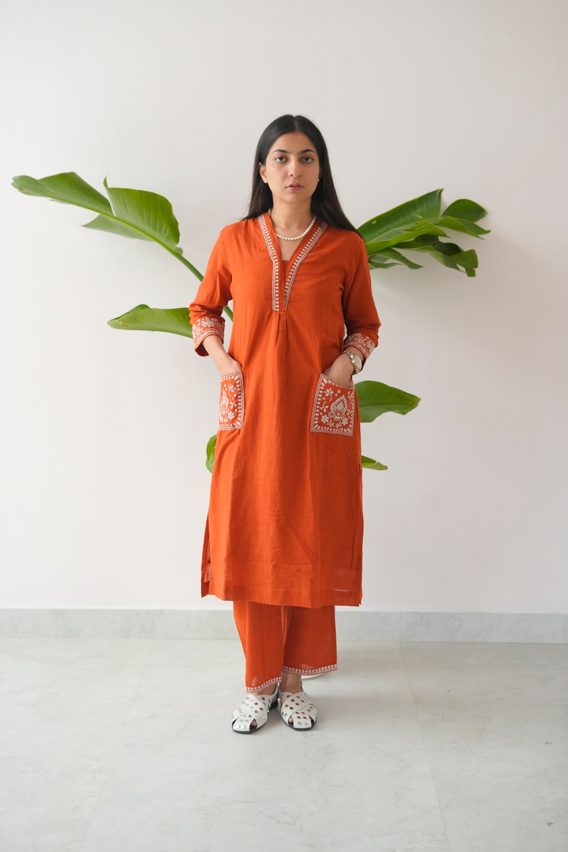 Woman wearing an orange kurta with white patterns against a white background