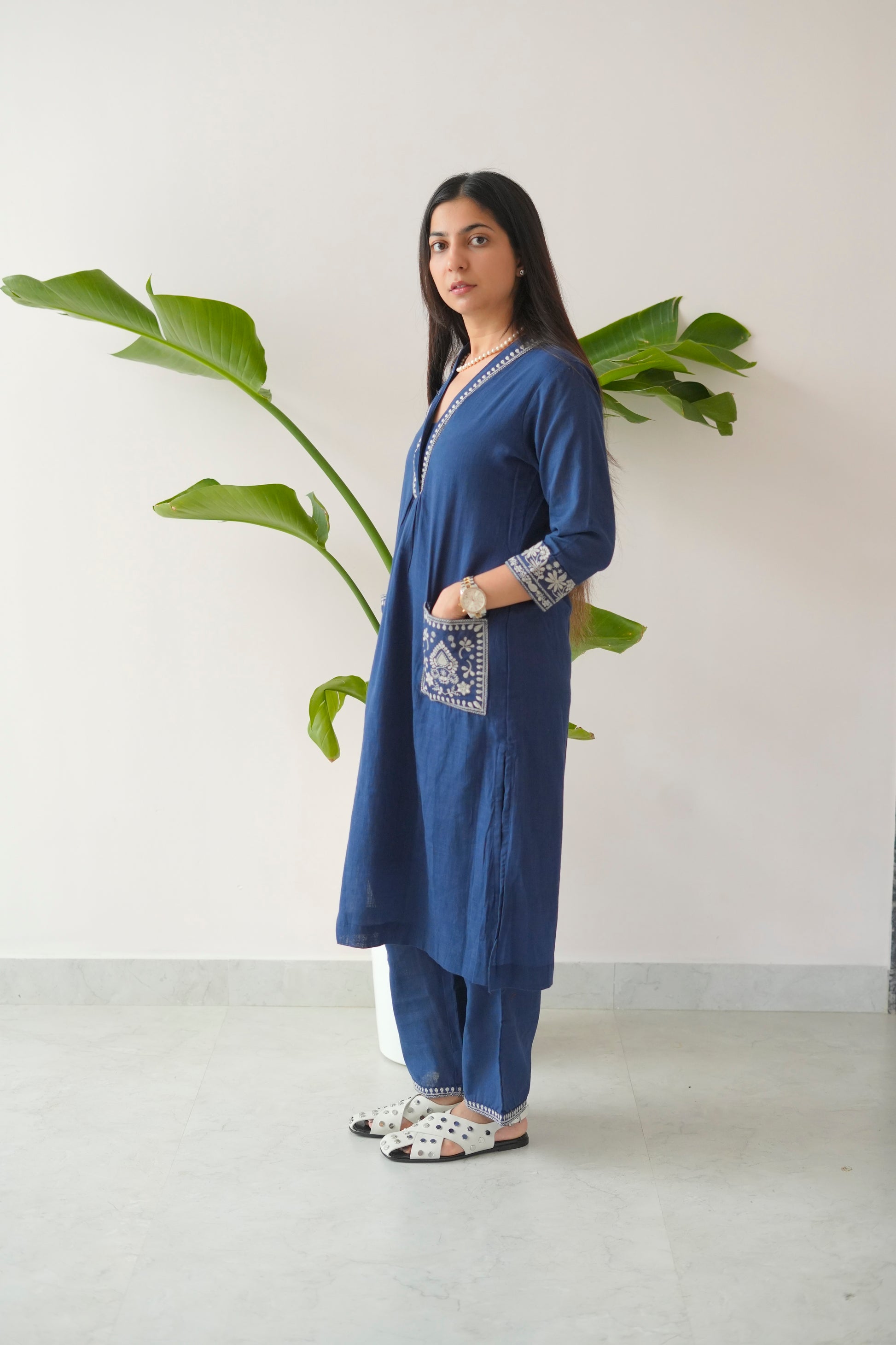 Woman wearing a blue traditional outfit with a white background and plant