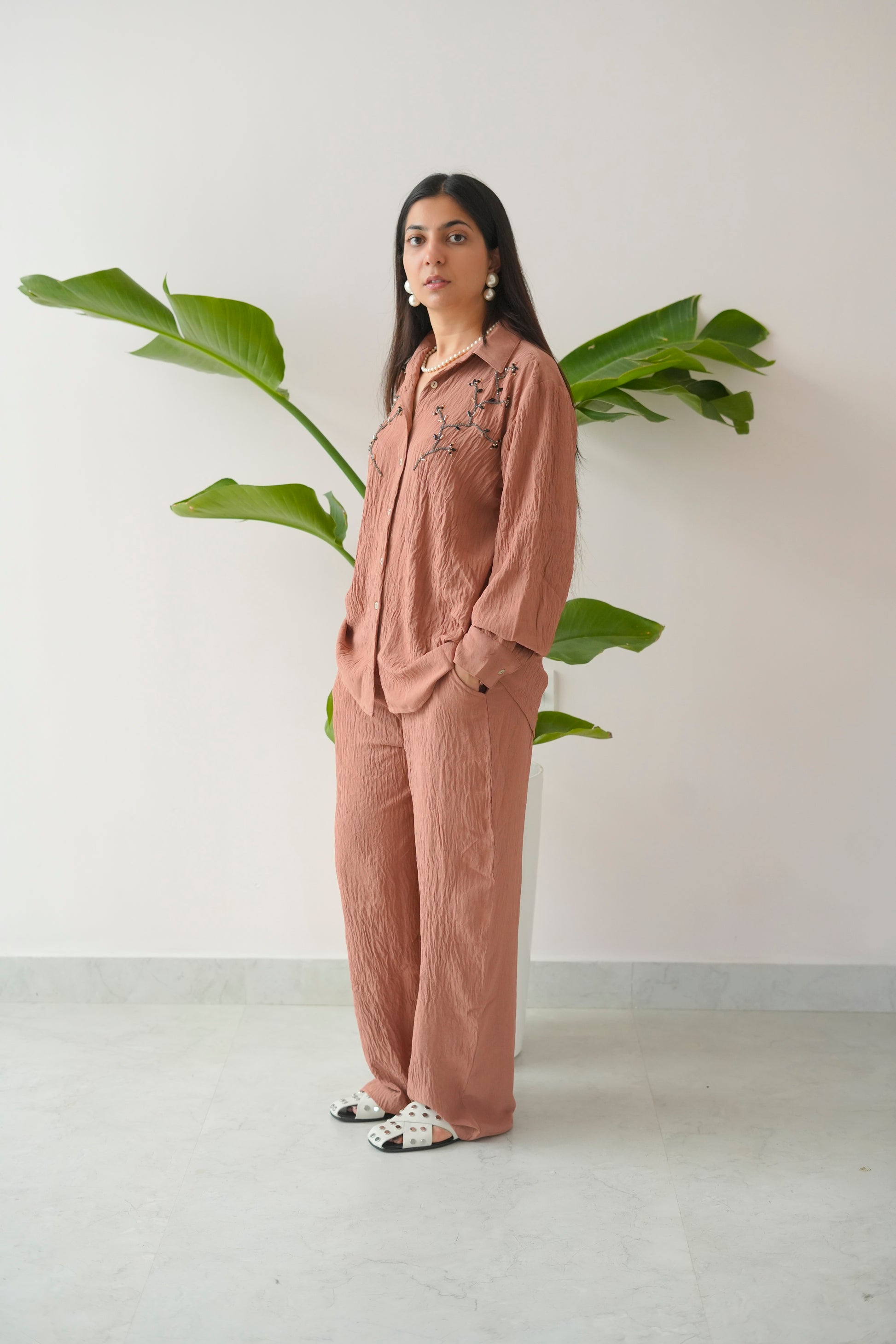 Woman in a pink outfit standing next to a plant against a white wall